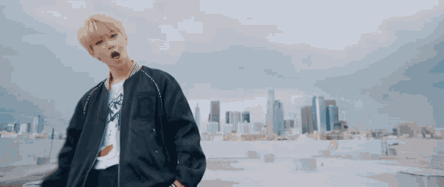 a young man in a black jacket is standing on a rooftop in front of a city skyline