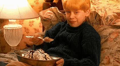 a young boy is sitting on a bed eating a bowl of ice cream .