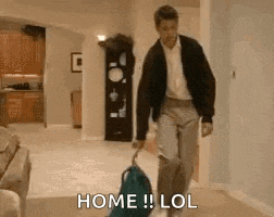 a man is walking with a suitcase in a living room and says `` home lol '' .