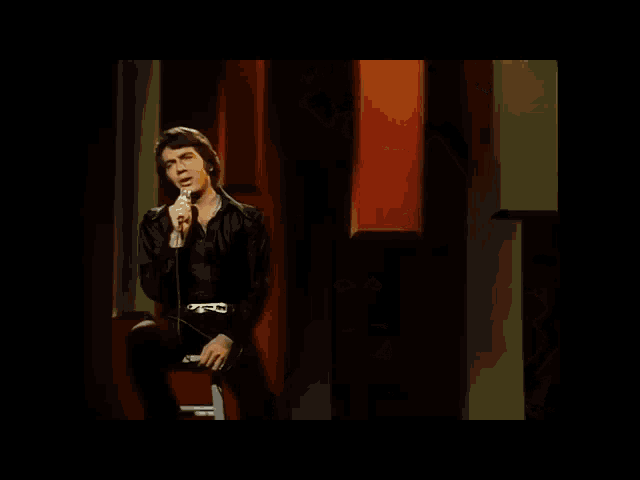 a man is singing into a microphone on a stage in a dark room .