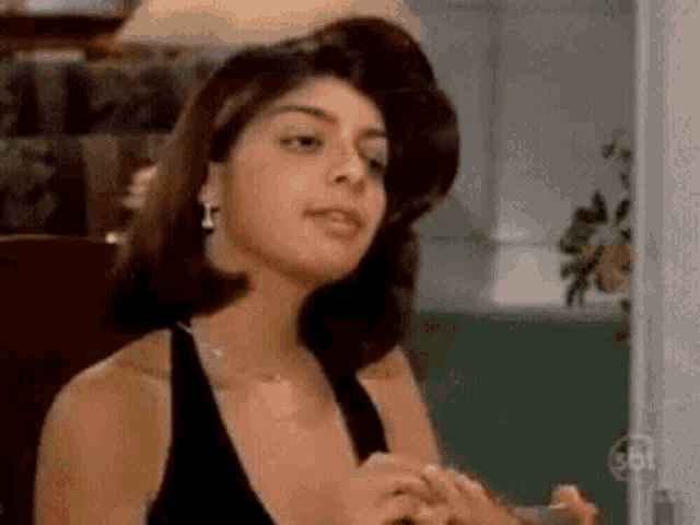 a woman in a black dress and earrings is sitting in a room .