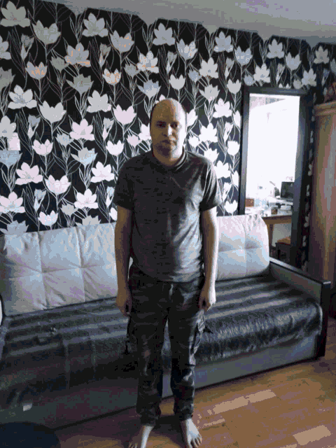 a man standing in front of a couch with a floral wallpaper on the wall