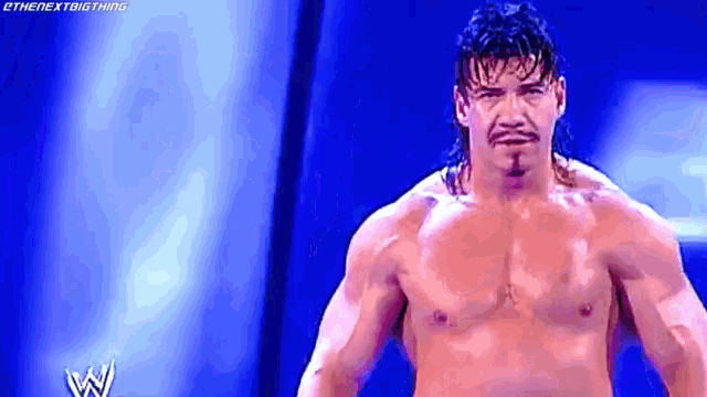 a shirtless wrestler with a mullet and mustache is standing in front of a blue background .