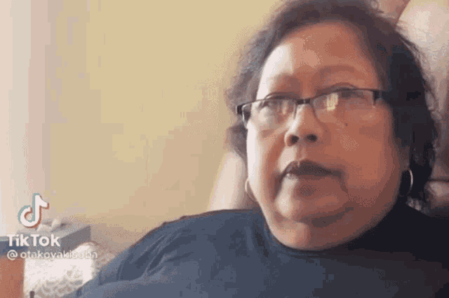 a woman wearing glasses and earrings is sitting in a chair and making a funny face .