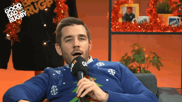 a man wearing a blue sweater is talking into a microphone with the words good bad and rugby written in the background