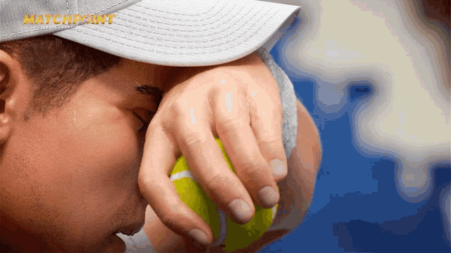 a man wearing a hat holds a tennis ball in front of his face with the word matchpoint in the corner