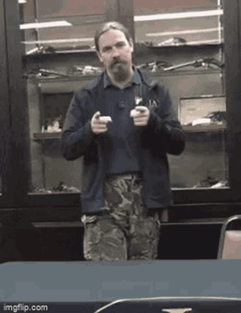 a man with a beard and mustache is standing in front of a glass cabinet holding a gun .