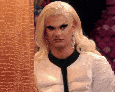 a drag queen with blonde hair and earrings is making a face