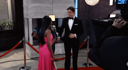 a man in a tuxedo is talking to a woman in a pink dress on a red carpet