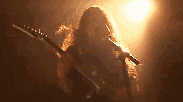 a person with long hair is playing a guitar in front of a microphone