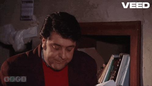 a man is sitting in front of a bookshelf and the word veed is on the bottom right