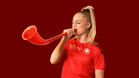 a woman wearing a red shirt with a swiss cross on it blows a red horn