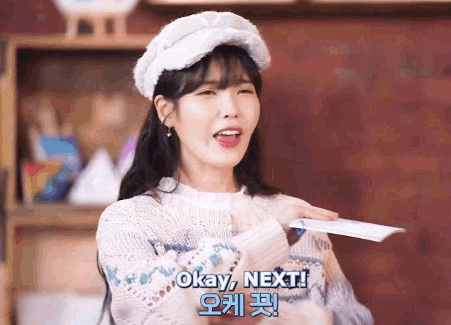 a woman wearing a white hat and a white sweater says " okay next "