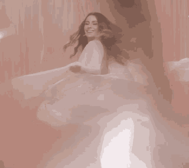 a woman in a long white dress is dancing in front of a pink curtain