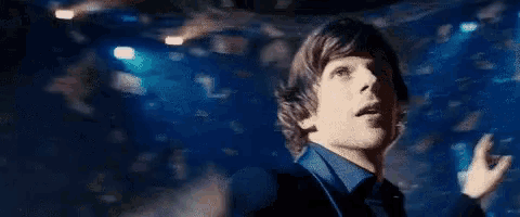 a man in a blue shirt is standing in a dark room with a lot of lights .