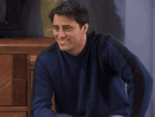 a man in a blue sweater is smiling and says yeah baby