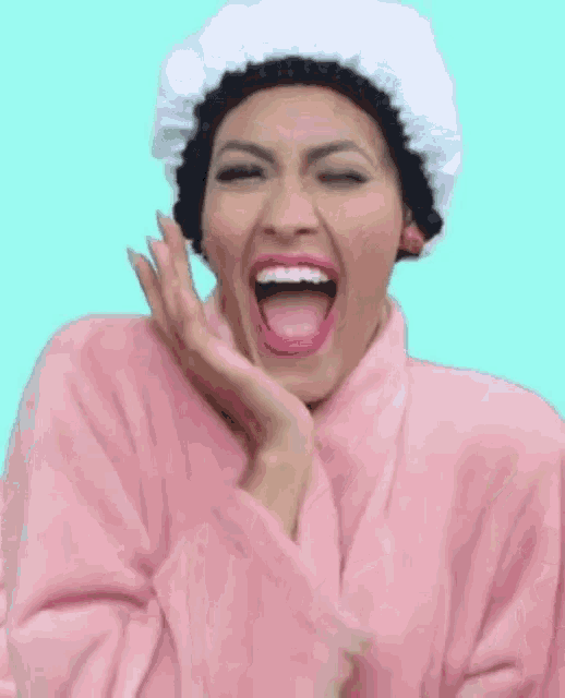 a woman wearing a pink robe and a shower cap is laughing with her mouth open .