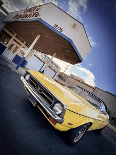 a yellow car is parked in front of scott 's automotive building