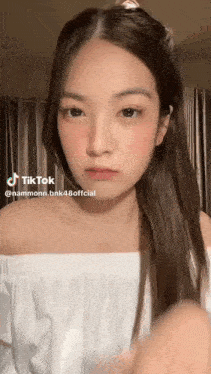 a young woman with long hair is wearing a white off the shoulder top and looking at the camera .