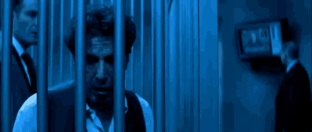 a man is behind bars in a jail cell with a blue background