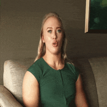 a woman in a green dress is sitting on a couch with her mouth open