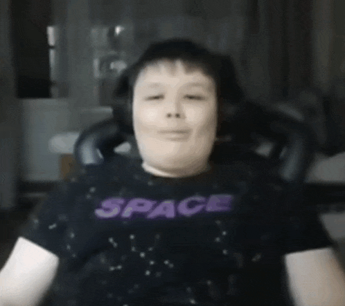 a young boy wearing a black shirt that says space is sitting in a chair .