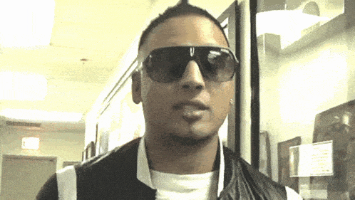 a man wearing sunglasses and a black vest looks at the camera