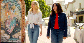 two women are walking down a sidewalk next to a painting on a wall .