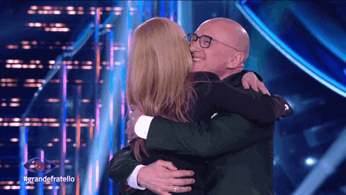 a man and a woman hugging on a stage with the words grandefratello on the bottom