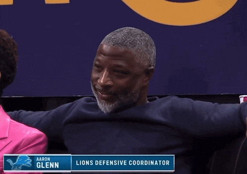 a man sitting in front of a sign that says aaron glenn lions defensive coordinator