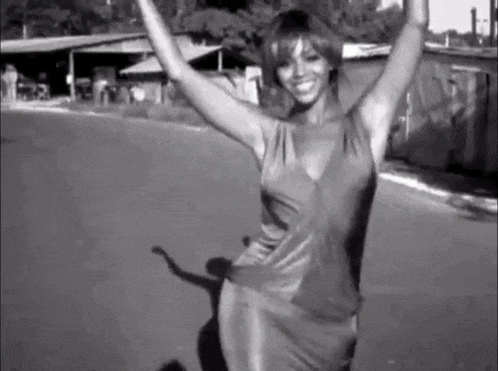 a black and white photo of a woman in a dress dancing on the street .