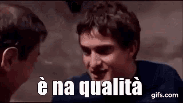 two men are talking to each other in a dark room and one of them is saying `` è na qualita '' .