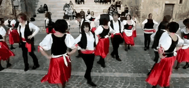 a group of people are dancing in red skirts and black vests