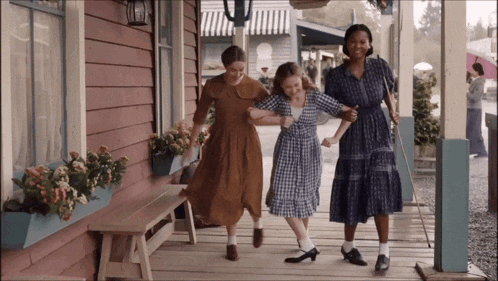 three women are walking on a porch holding hands and one has a cane
