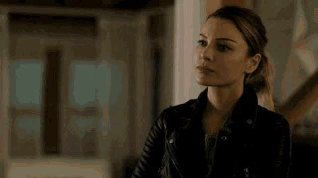 a woman in a black leather jacket is standing in a room