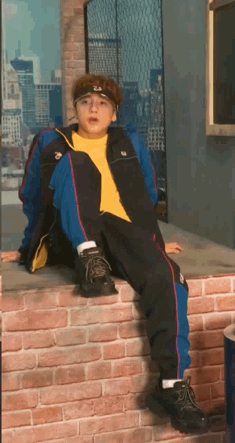 a young boy is sitting on a brick wall wearing a fila jacket