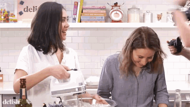 two women in a kitchen with a sign that says delish in the corner