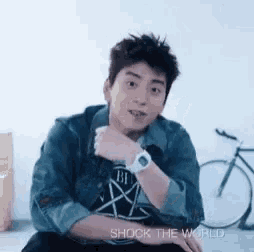 a man wearing a watch and a denim jacket is sitting on the floor .