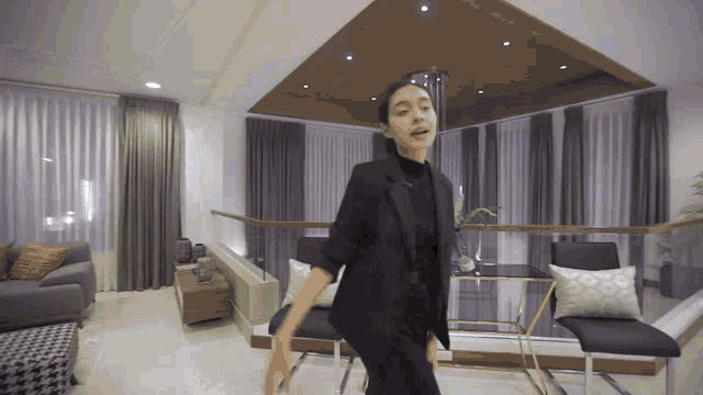 a woman in a black suit stands in a living room
