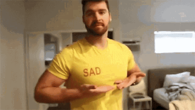 a man wearing a yellow shirt with the word sad on it is standing in a room .
