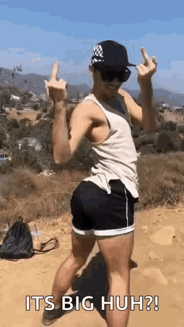a man in a tank top and shorts is giving the middle finger while standing on a dirt hill .