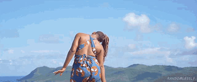a woman with braids is standing on top of a hill overlooking the ocean .