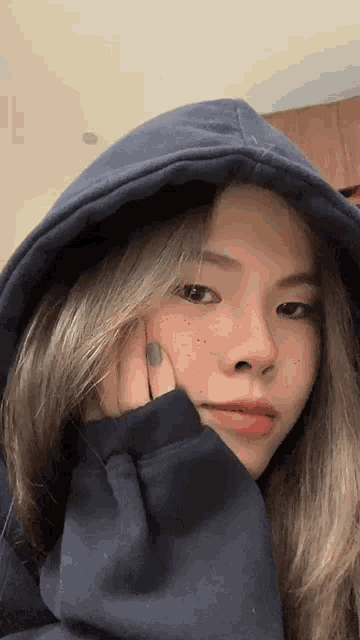 a woman wearing a blue hoodie has her hand on her chin