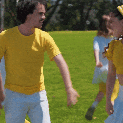 a man in a yellow shirt is holding hands with a woman in a blue dress