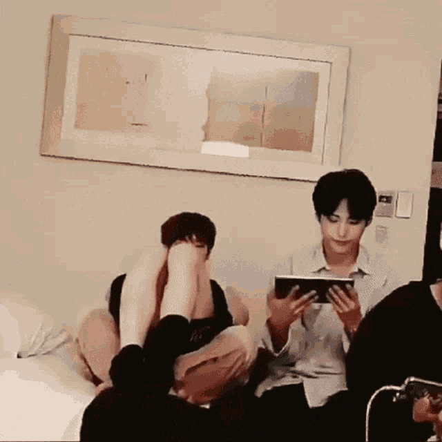 a group of people are sitting on a bed with their feet up and one of them is holding a tablet