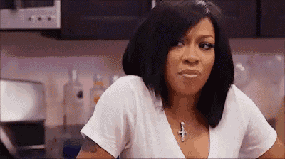 a woman is making a funny face in a kitchen while wearing a white shirt and a cross necklace .