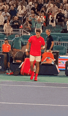 a man in a red shirt and white shorts stands on a tennis court in front of a crowd