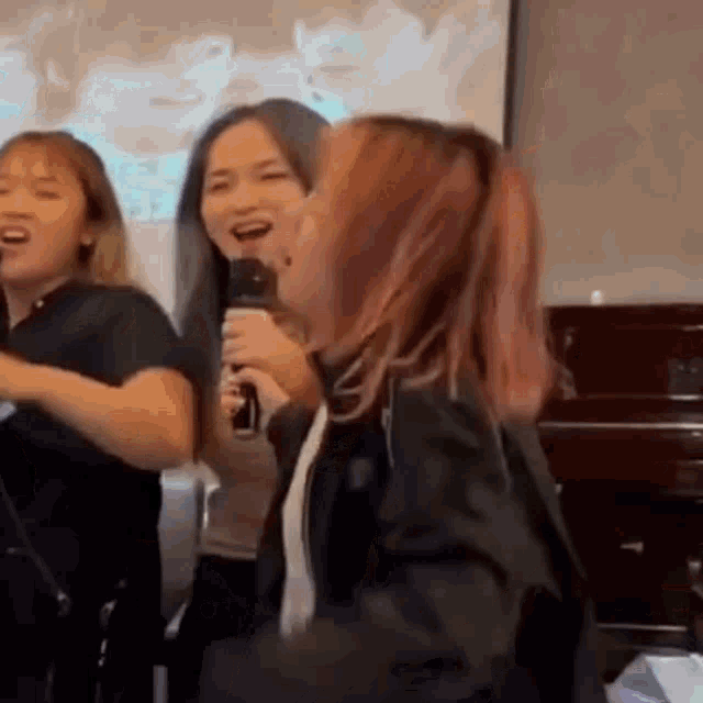 a group of women are singing into microphones while standing next to each other .
