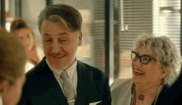 a man in a suit and tie and a woman in glasses are laughing .