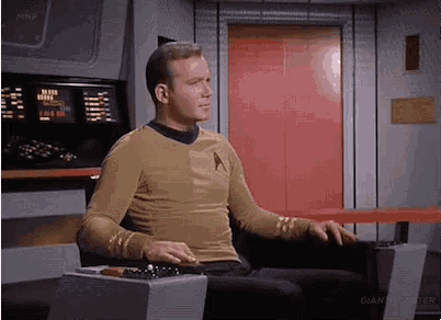 a man in a star trek uniform is sitting in a chair in front of a red door .